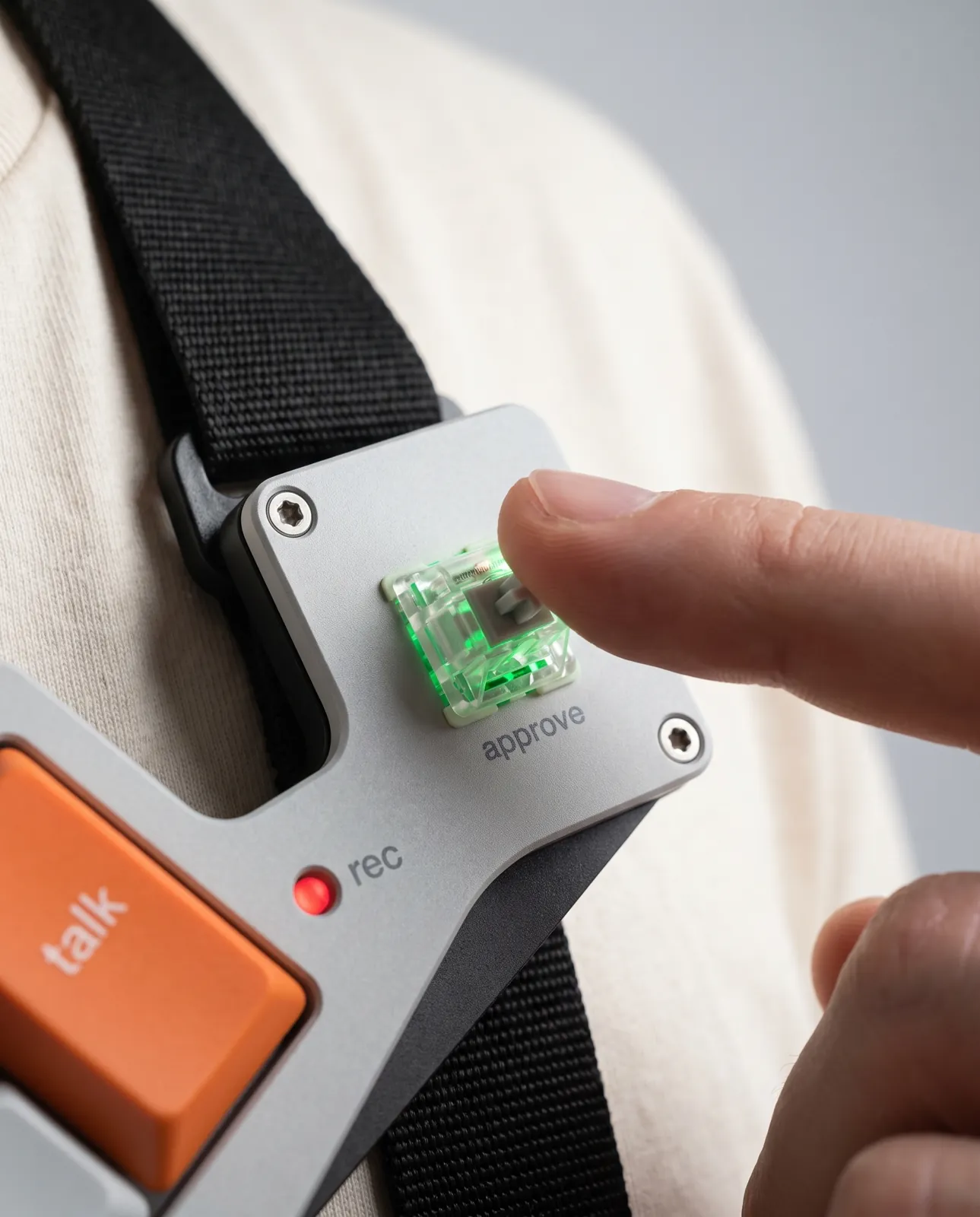 A fingertip about to press the green-lit approve keyswitch on the chest-mounted panel.