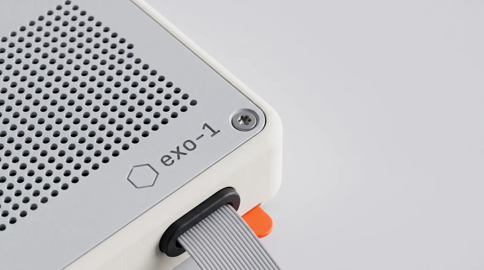 Close-up of a corner of the Pi case: the grey perforated lid, a torx screw, a small hexagon outline and exo-1 printed in lowercase, the grey ribbon cable leaving through a black grommet, and an orange pull-tab.